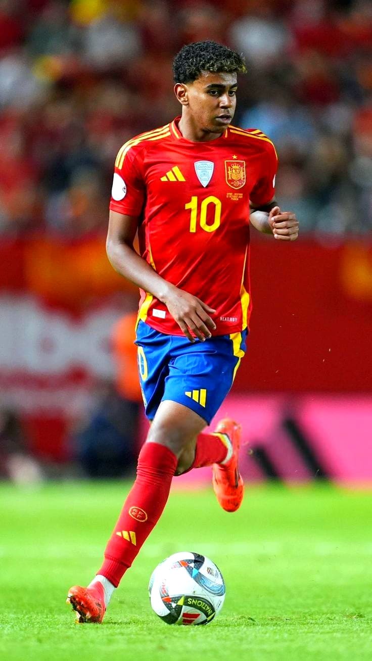 A soccer player in a red and yellow Spain jersey with number 10 is dribbling a ball on the field. The background is blurred, showing an audience in a stadium, perfect for watching live through IPTV Netherland.